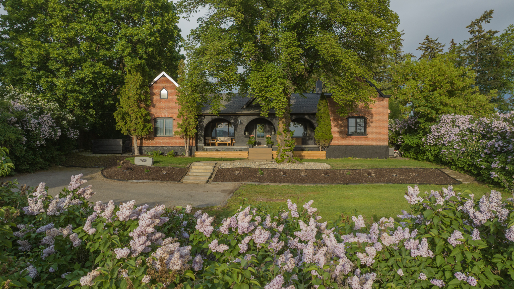 Front elevation framed by lilacs and mature trees